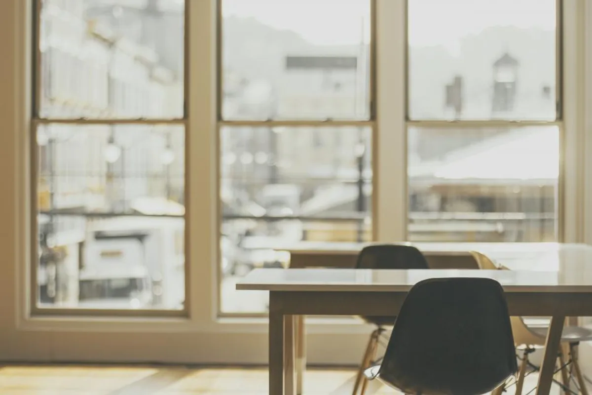 An empty chair at a table in front of tall windows filled with soft daylight