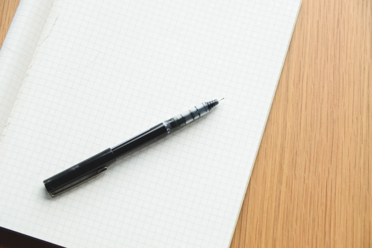 A black pen lying on a blank squared notebook on a wooden desk